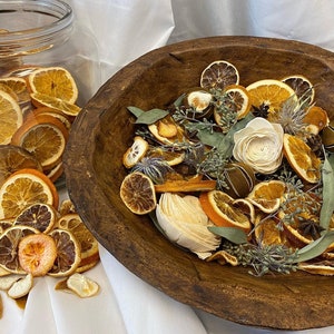 Könnte beinhalten: Eine Holzschale gefüllt mit getrockneten Orangenscheiben, Eukalyptusblättern und anderen natürlichen Elementen. Die Schale steht auf einer weißen Oberfläche, und um sie herum liegen weitere getrocknete Orangenscheiben.