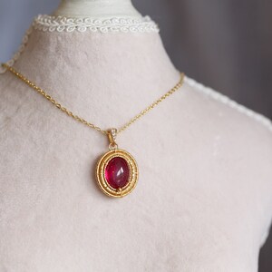 May include: A gold chain necklace with a pendant featuring a large, oval-shaped, red gemstone surrounded by a gold filigree design.