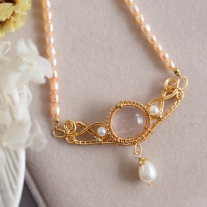 Puede incluir: Un delicado collar de oro con un colgante de cuarzo rosa y detalles de perlas. El collar est&aacute; hecho con alambre envuelto alrededor de las piedras y presenta una gota de perla.