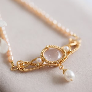 Puede incluir: Un delicado collar de oro con un colgante de cuarzo rosa y detalles de perlas. El collar presenta un dise&ntilde;o de alambre envuelto con una delicada gota de perla.