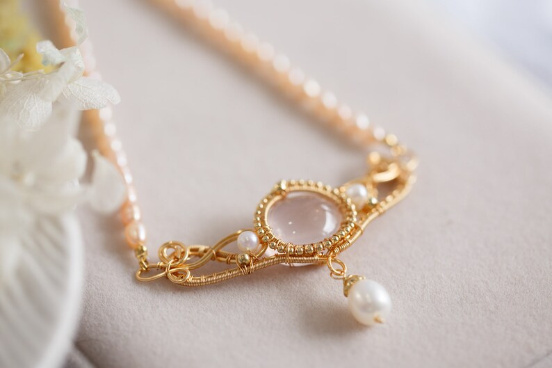 Puede incluir: Un delicado collar de oro con un colgante de cuarzo rosa y detalles de perlas. El collar presenta un dise&ntilde;o de alambre envuelto con una delicada gota de perla.