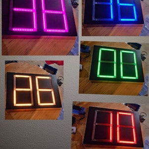May include: Five different versions of a scoreboard with two rectangular displays. The scoreboards are black with white frames around the displays. The displays are lit up with different colors: pink, blue, green, orange, and red.
