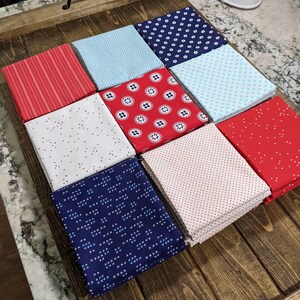 May include: A wooden tray with nine fabric squares in various patterns and colors, including red, white, blue, and light blue. The fabrics are arranged in a grid pattern.