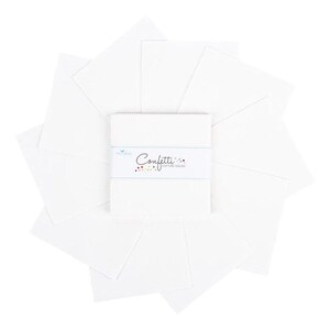 May include: A stack of white cotton squares arranged around a smaller stack of squares. The smaller stack has a label that reads "Confetti Cotton Solids" in a script font. The label has a blue line and colorful dots.