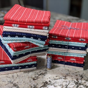 May include: A stack of red, white, and blue fabric squares with different patterns. The fabric is bundled with twine and there is a spool of twine next to the fabric.
