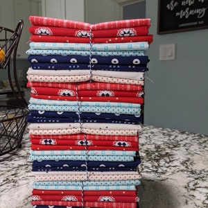 May include: A stack of fabric squares in red, white, and blue with various patterns, including polka dots, stripes, and geometric designs. The fabric is bundled together with twine.