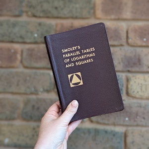 May include: A burgundy leather-bound book titled "Smoley's Parallel Tables of Logarithms and Squares" with a gold triangle and square symbol on the cover.