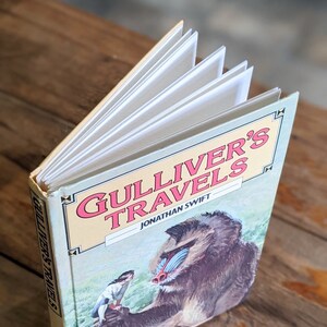 May include: A closed book titled "Gulliver's Travels" by Jonathan Swift. The cover features a colorful illustration of a mandrill monkey and a small human figure.