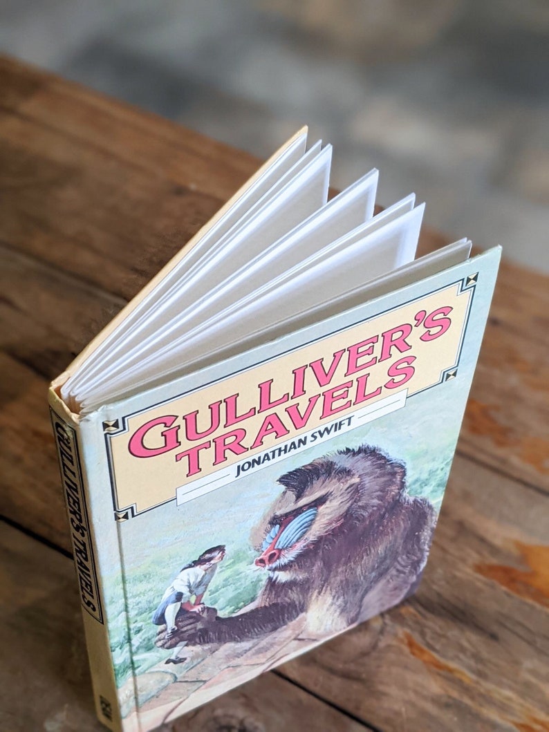 May include: A closed book titled "Gulliver's Travels" by Jonathan Swift. The cover features a colorful illustration of a mandrill monkey and a small human figure.