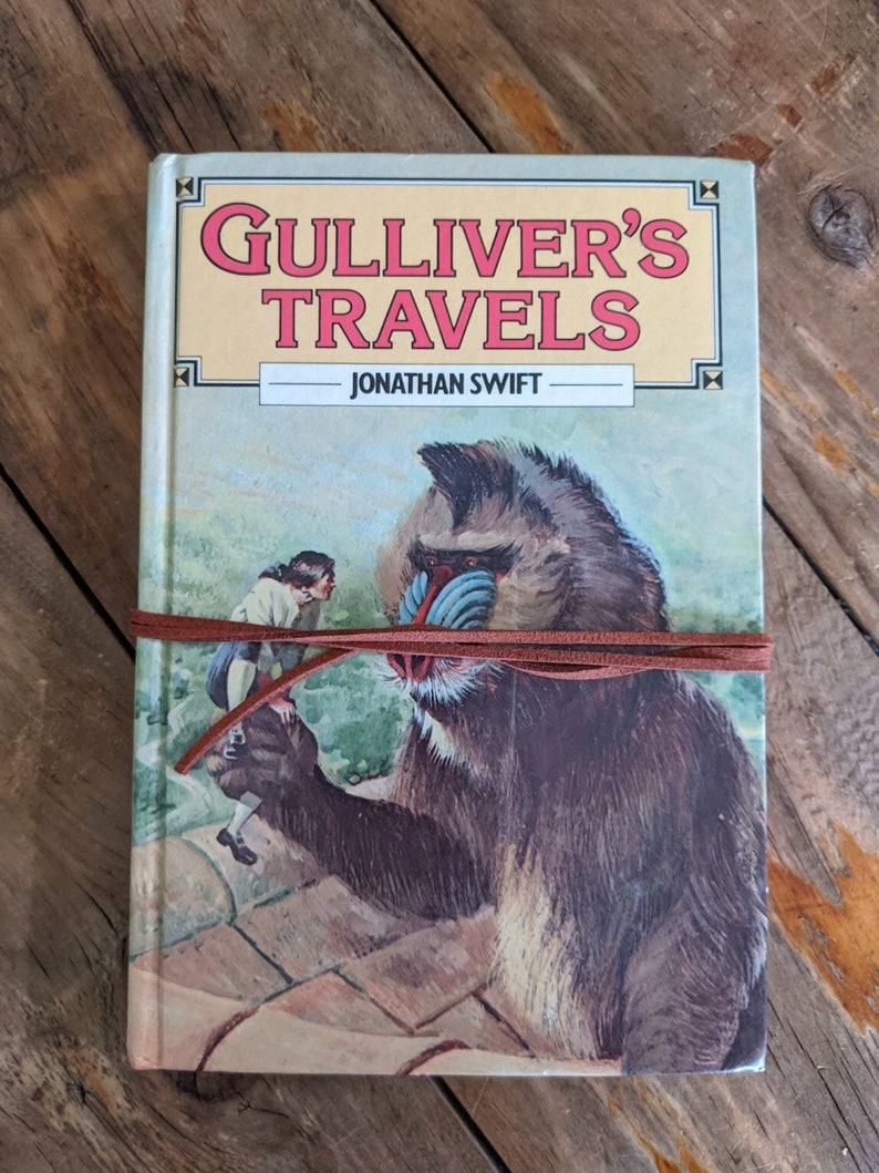 May include: A vintage hardcover book titled "Gulliver's Travels" by Jonathan Swift. The cover features an illustration of a large, brown, furry creature with a blue face and a small human figure standing on a stone surface.