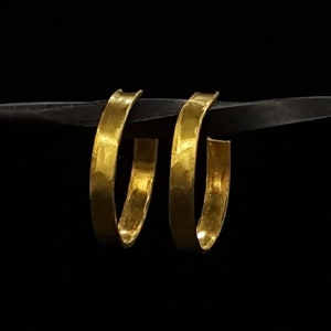 May include: A pair of gold hoop earrings. The earrings are made of thick, hammered metal and have a simple, elegant design.