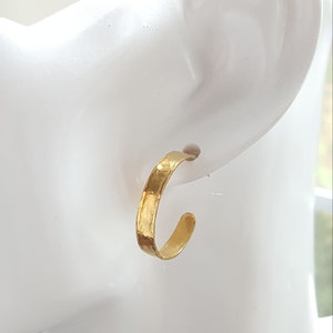 May include: Gold hoop earrings with a hammered texture. The earrings are shown on a white mannequin head.