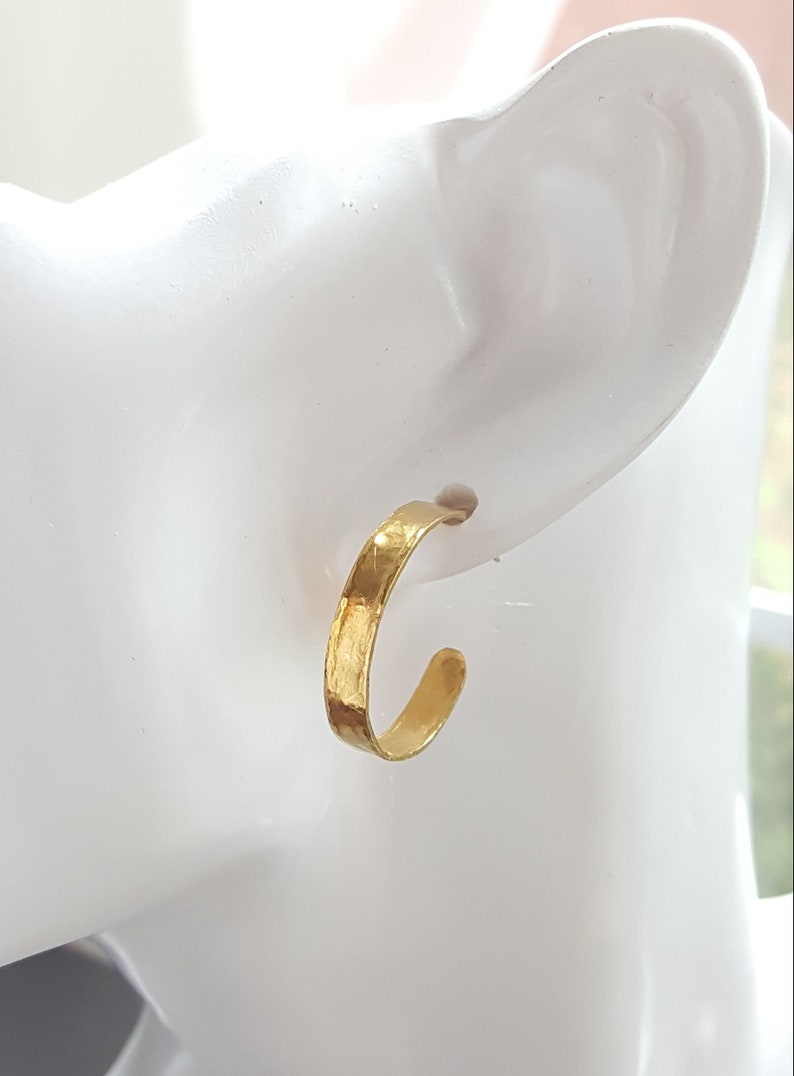 May include: Gold hoop earrings with a hammered texture. The earrings are shown on a white mannequin head.