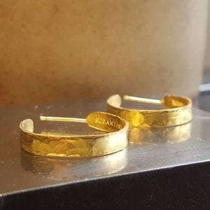 May include: A pair of gold hoop earrings with a hammered texture. The earrings are marked "Bizantino" on the back.