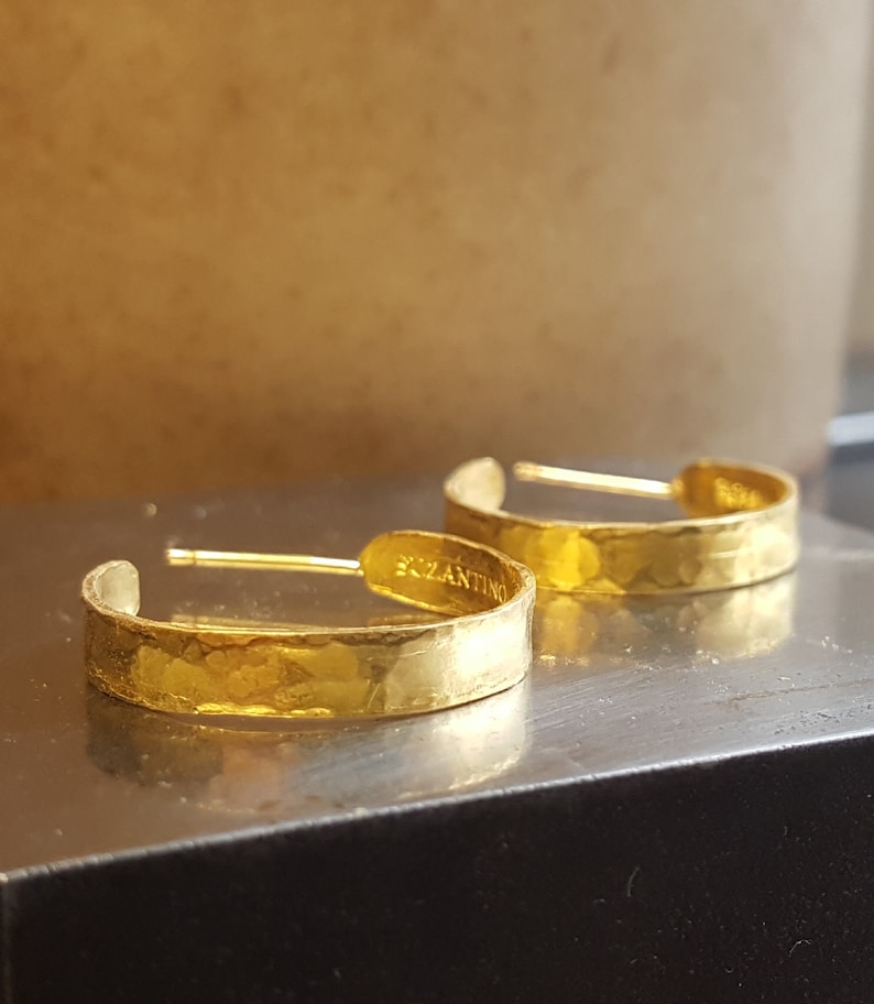 May include: A pair of gold hoop earrings with a hammered texture. The earrings are marked "Bizantino" on the back.