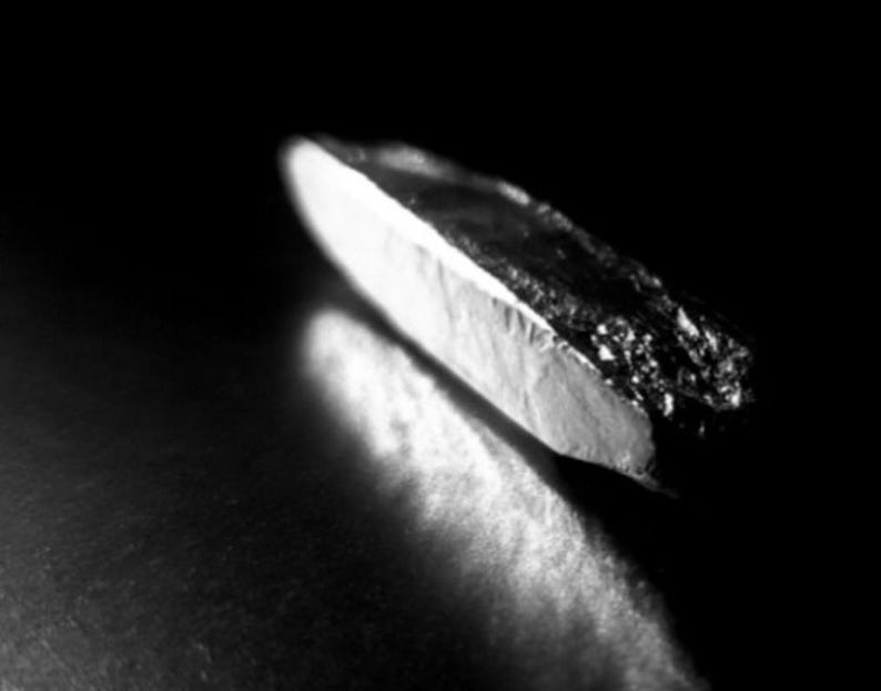 May include: A monochrome image showing a small, angular object with a bright, white edge and a dark, textured surface. The object is set against a dark, blurred background, creating a high-contrast effect.