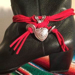 May include: Black leather boots with a red suede wrap and silver heart-shaped charms. The boots have a low heel and are decorated with tassels.