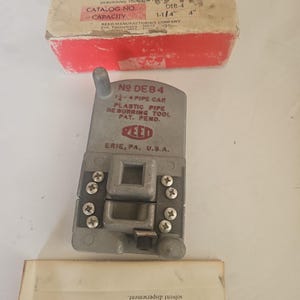 May include: A grey metal Reed No. DEB4 plastic pipe deburring tool with a capacity of 3.175 cm to 10.16 cm. The tool features a rectangular body with multiple screws and is accompanied by its original red and white cardboard box and instruction manual.