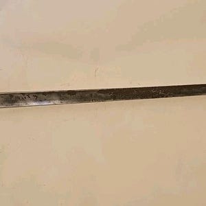 May include: A vintage bayonet with a long, slender, dark metal blade. The bayonet has a curved section and a cylindrical handle with a ring. The blade shows signs of wear and age, with a slightly dull finish.
