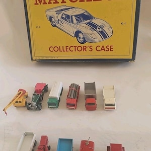 May include: A yellow and blue rectangular Matchbox collector's case with a graphic of a race car, accompanied by eleven assorted die-cast toy vehicles including trucks, a crane, and construction equipment in various colors like red, green, and blue.