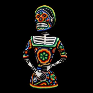 Puede incluir: Una figura de esqueleto de cuentas coloridas con una cabeza de calavera, vestida con un vestido estampado en verde, naranja y azul. La figura está hecha de cuentas y tiene un estilo tradicional mexicano del Día de Muertos.
