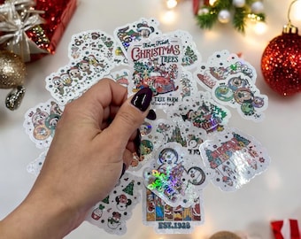 May include: A selection of Christmas stickers with cartoon characters and festive designs. The stickers feature Mickey Mouse, Christmas trees, and the text "From Fresh Christmas Trees Tree Farm". The stickers are on a white surface with Christmas decorations.