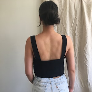 May include: A black sleeveless top with a square neckline and wide straps. The top is cropped and shows the model's back.
