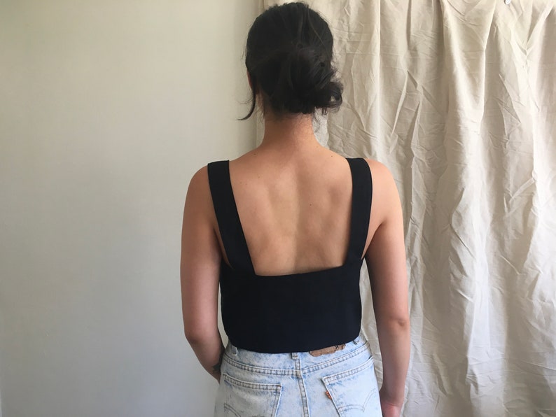 May include: A black sleeveless top with a square neckline and wide straps. The top is cropped and shows the model's back.