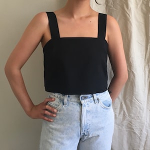 May include: A black cropped tank top with wide straps. The top is made of a smooth, lightweight fabric. The model is wearing the top with light blue denim jeans.
