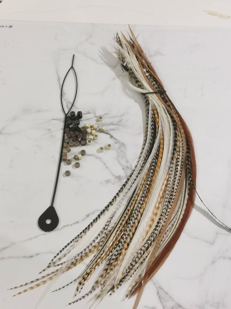 May include: A bundle of brown, white, and black feathers with a black string tied around them. There are also a variety of small, round, brown and beige beads scattered on a white surface.