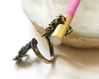 May include: A gold dragon ring with a pink and gold cigarette holder. The ring and holder are on a white agate dish.