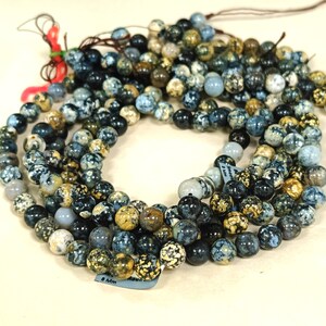 May include: A strand of blue, black, and gold speckled round beads. The beads are approximately 8 mm in diameter. The beads are strung on a clear string.
