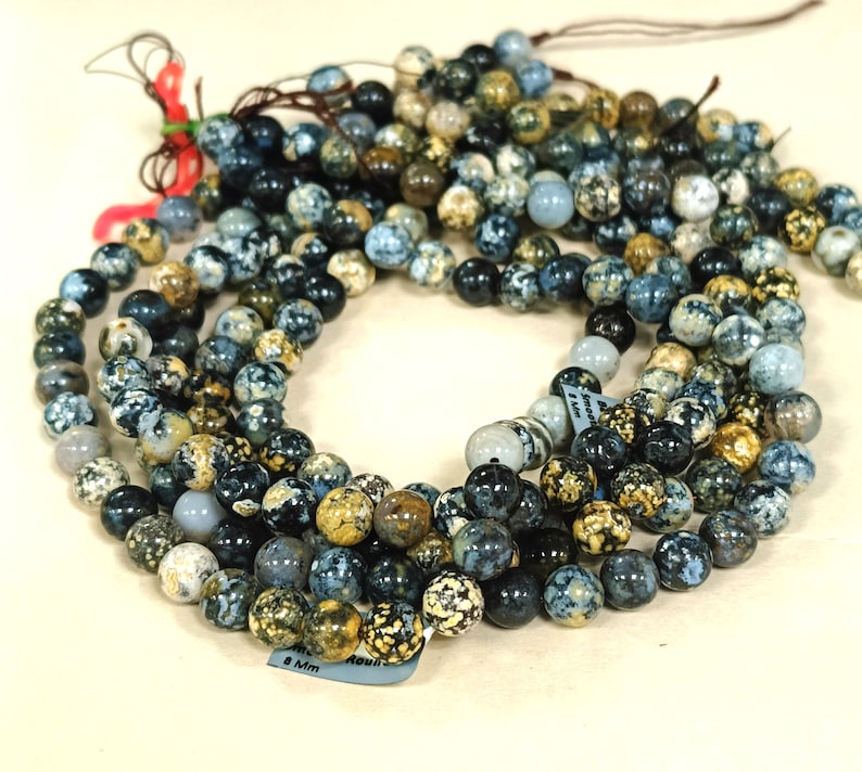 May include: A strand of blue, black, and gold speckled round beads. The beads are approximately 8 mm in diameter. The beads are strung on a clear string.