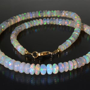 May include: A white opal beaded necklace with a gold clasp. The necklace is made of round, faceted opal beads that are iridescent and have a rainbow of colors.