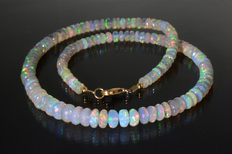 May include: A white opal beaded necklace with a gold clasp. The necklace is made of round, faceted opal beads that are iridescent and have a rainbow of colors.