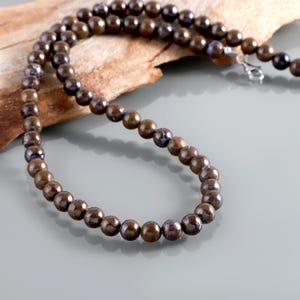 May include: A brown beaded necklace with iridescent purple accents. The necklace is made of round beads and is strung on a silver chain.