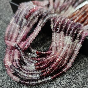 May include: A strand of pink and purple gemstone beads. The beads are faceted and have a slightly irregular shape. The beads are strung on a clear thread.