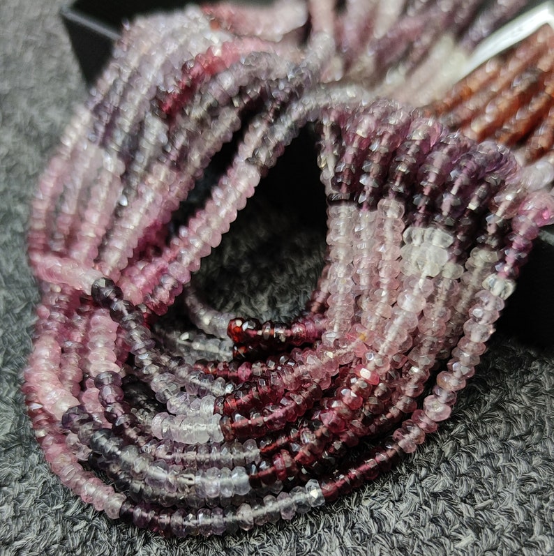 May include: A strand of pink and purple gemstone beads. The beads are faceted and have a slightly irregular shape. The beads are strung on a clear thread.