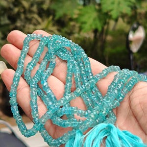 May include: A strand of light blue aquamarine beads, faceted and with a slightly irregular shape. The beads are strung on a thin cord and have a tassel at the end.