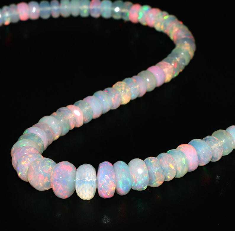 May include: A strand of iridescent opal beads in shades of white, pink, and blue. The beads are faceted and have a slightly irregular shape. The strand is approximately 18 inches long.