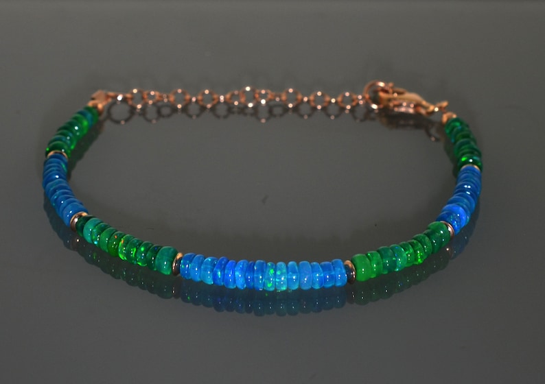 Pu&ograve; includere: Un braccialetto con perline di opale verde e blu con una chiusura dorata.