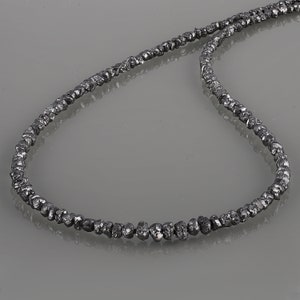 May include: A necklace made of black rough diamonds. The necklace is made of a single strand of diamonds that are strung together.
