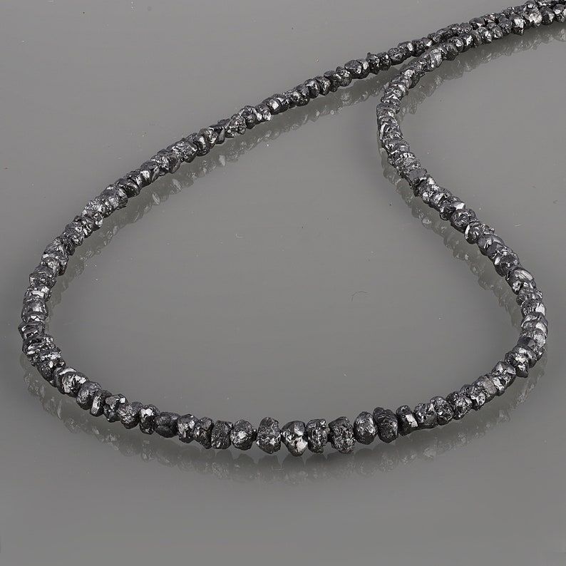 May include: A necklace made of black rough diamonds. The necklace is made of a single strand of diamonds that are strung together.