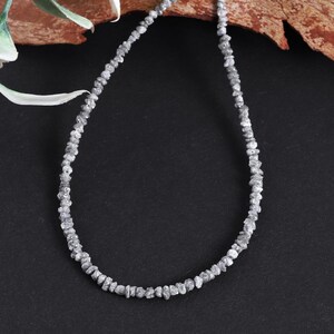 May include: A silver necklace made of rough, uncut diamonds. The necklace is on a black background.