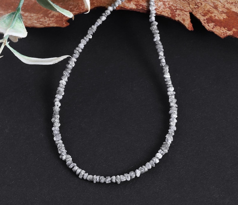 May include: A silver necklace made of rough, uncut diamonds. The necklace is on a black background.