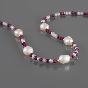 May include: A white pearl and ruby gemstone necklace. The necklace is made with small, faceted ruby beads and white pearls. The pearls are strung on a gold chain.