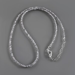 May include: A silver necklace made of small, rough, grey diamonds. The necklace has a lobster clasp closure.
