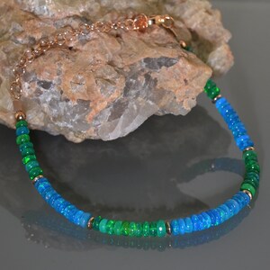 Pu&ograve; includere: Un braccialetto delicato realizzato con perline di opale blu e verde alternate, collegate da una catena in oro rosa.