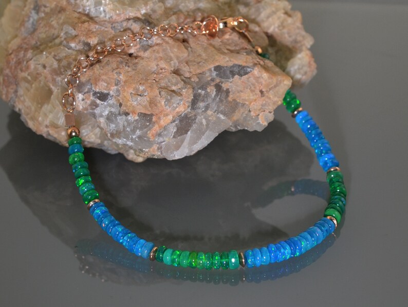 Pu&ograve; includere: Un braccialetto delicato realizzato con perline di opale blu e verde alternate, collegate da una catena in oro rosa.