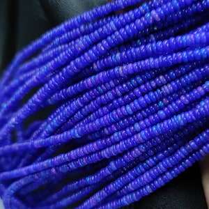 以下が含まれることがあります： 青いオパールビーズのストランド。各ビーズは小さく丸く、わずかに虹色の輝きがあります。